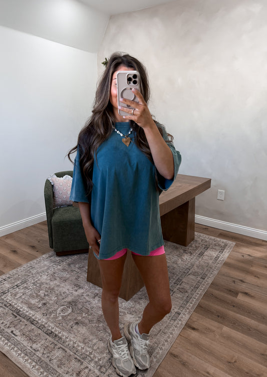 Person taking a mirror selfie wearing a teal dress with pink accents in a room.