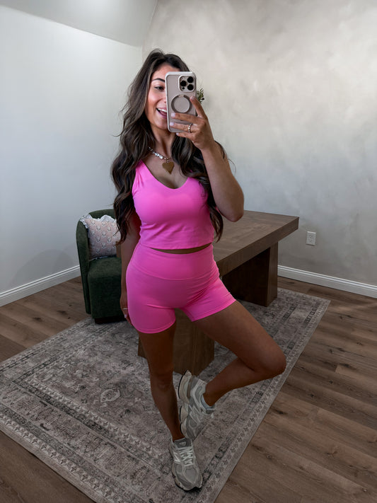 Woman taking a mirror selfie wearing a pink athletic outfit in a home setting.