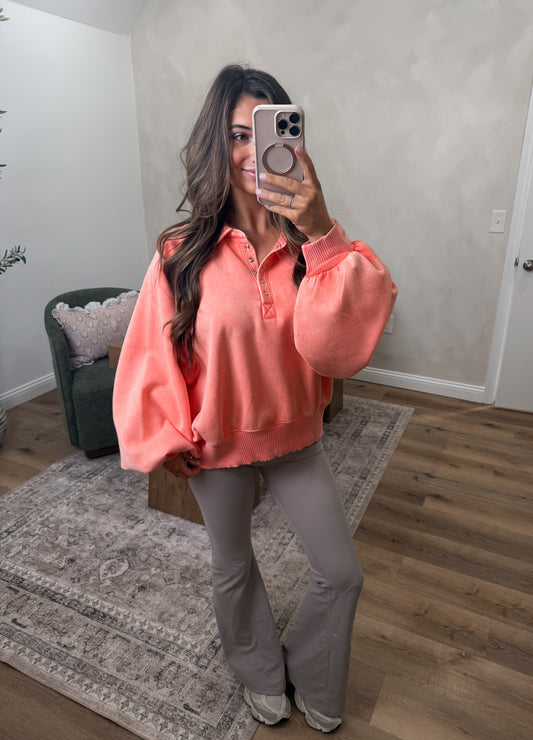 Woman taking a mirror selfie wearing a coral blouse and gray pants in a room with a rug and chair.