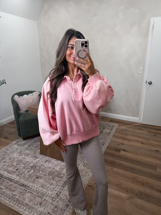 Woman taking a mirror selfie wearing a pink sweater and gray pants in a room with a green chair and white walls.