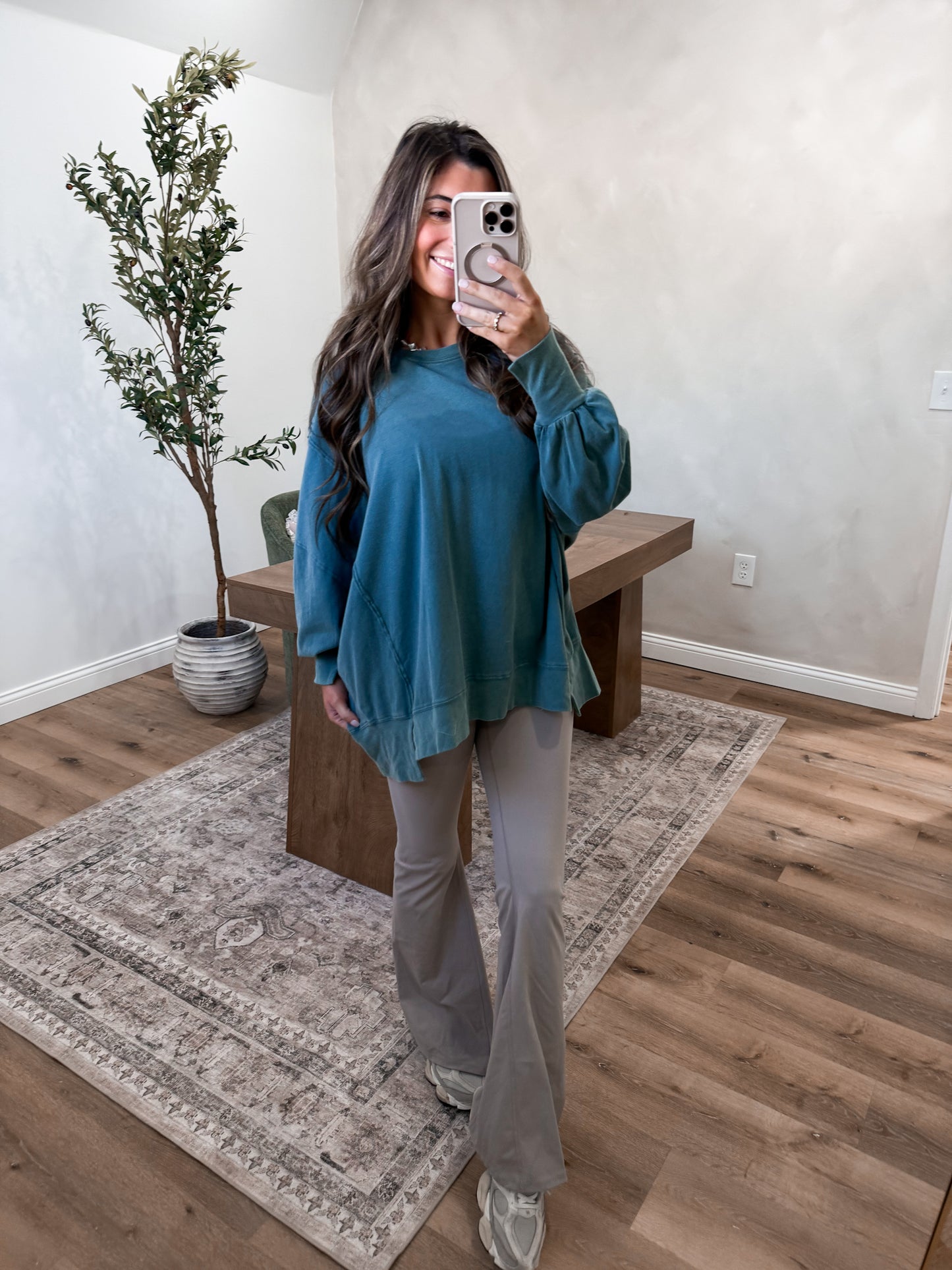 Woman taking a mirror selfie in a room with wooden flooring and a plant.