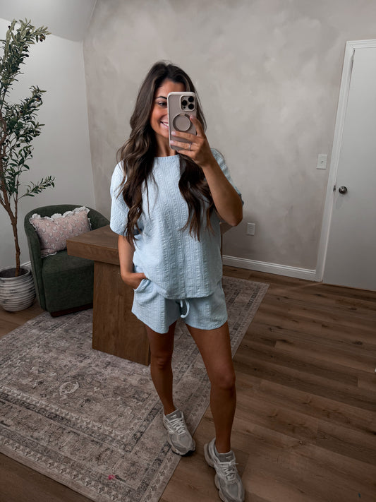 Woman taking a mirror selfie in a casual outfit in a living room.