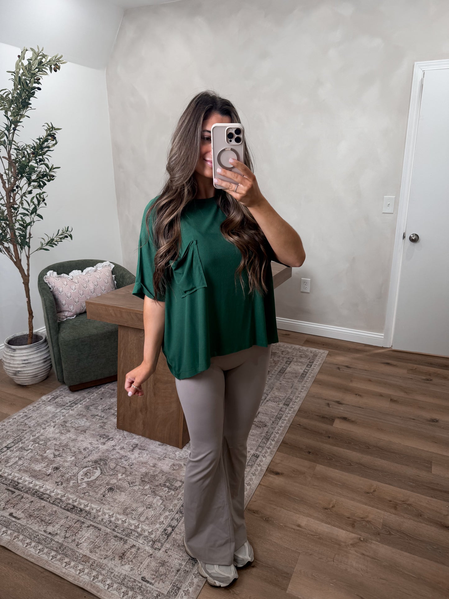 Women in a room wearing a green pocket shirt, grey leggings and tennis shoes. 