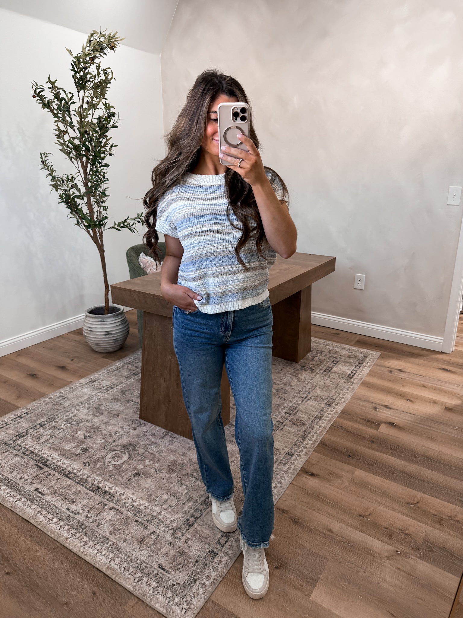 Woman taking a mirror selfie in a room with wooden flooring and a plant.