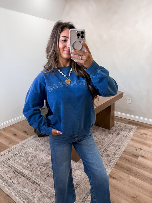 Person wearing a blue sweatshirt and jeans taking a mirror selfie in a room.