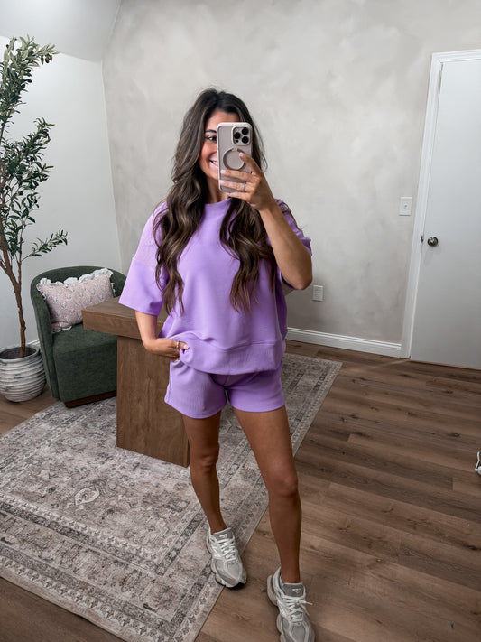 Person taking a mirror selfie wearing a purple outfit in a living room.
